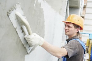 builder worker plastering facade of high-rise building with putty knife - use our how to plaster a wall guide to help you undertake a DIY wall plastering project